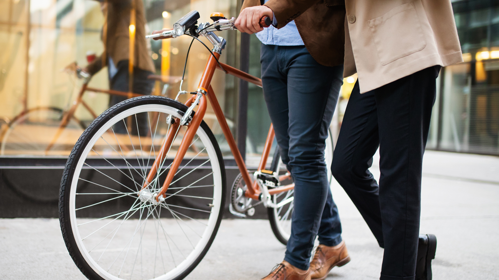to mænd går og taler med en kaffe i hånden. Den ene mand har en cykel med sig