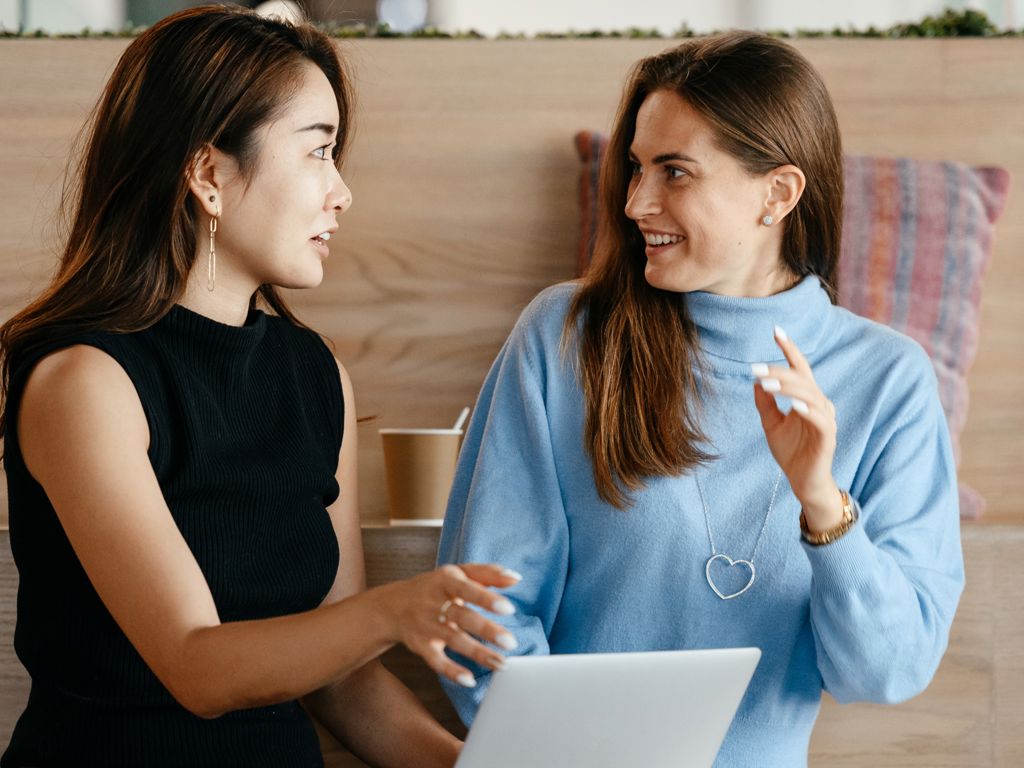 to unge kvinder sidder og taler sammen omkring en computer