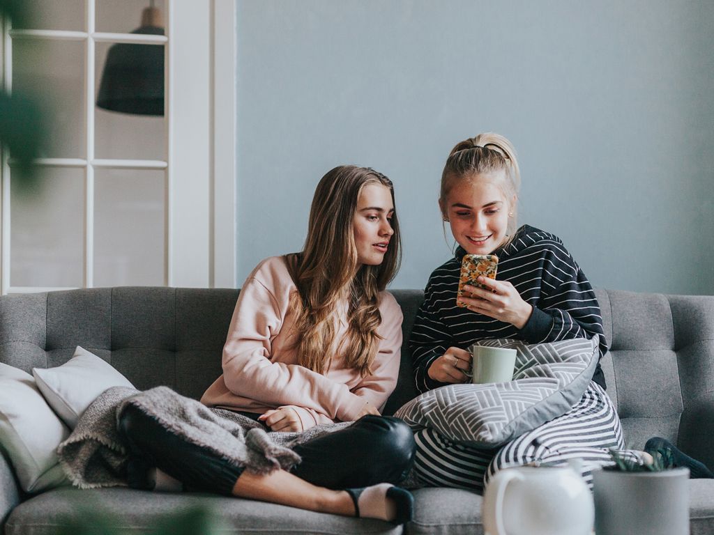 to unge kvinder sidder i en sofa og kigger på en mobil